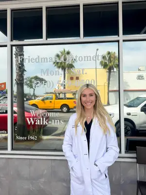 A woman in a white lab coat stands in front of a Friedman Optometry storefront.