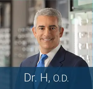 Dr. H, O.D. smiles in a suit at an optometrist's office