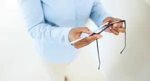 A person is adjusting a pair of glasses with black lenses.