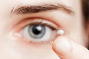 A woman holding a contact lens in front of her eye.