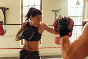 A woman in a black sports bra is practicing boxing with a man in a gym