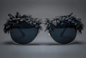 A pair of sunglasses with black lenses and blue and black feathers on the arms
