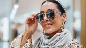 A smiling woman wearing sunglasses and a scarf in a mall
