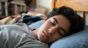 A man sleeping in a bed with his eyes closed and wearing a gray shirt