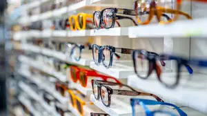 A display of various colored and styled eyeglasses arranged on white shelves in a store.