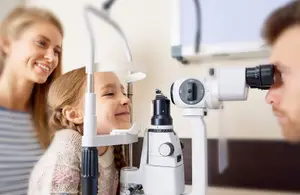 A girl wearing a white sweater is having her eyes examined by a doctor with a phoropter device in an optical shop