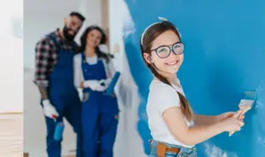 Family painting a blue wall with a girl holding a paintbrush and her parents behind her.