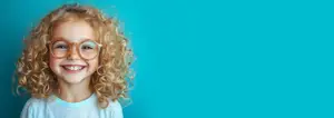 Smiling little girl with curly blonde hair wearing glasses against a blue background