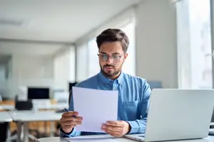 business man sitting at a desk working with a laptop and a paper