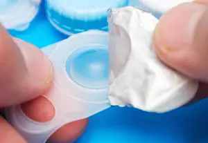 A person holding a contact lens case and a foil-wrapped lens