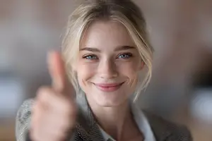 Close up of a smiling woman wearing a business suit and blazer and giving a thumbs up gesture