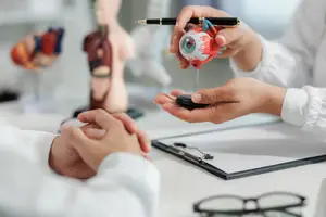 An optometrist shows a model of an eye to a patient during an eye exam.