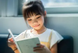 A smiling little girl reading a book on a couch with sunlight shining on her face