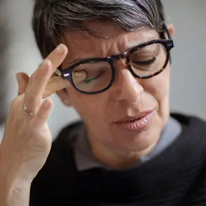 A person wearing glasses and a ring is looking down and seems to be touching their glasses with their right hand.