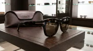 A pair of Tom Ford sunglasses is displayed on a wooden table with a leather case beside it in a store setting