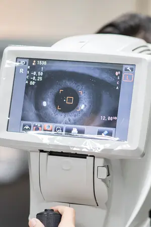 A white machine with a digital screen displaying an eye image is being held by a person with their right hand.