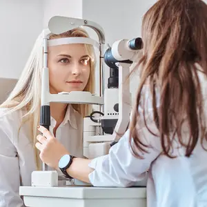 A woman with blonde hair is getting her eyes checked by a doctor in a white coat in a room with white walls.