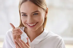 A woman in a white shirt holding a container of contact lenses and smiling