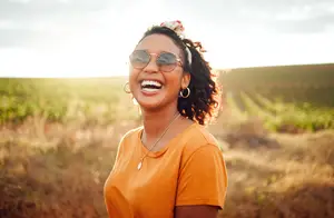 A woman smiling and laughing while standing in a field with dry grass