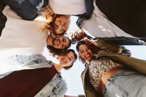 A group of friends, a man and three women, are smiling and posing for a photo in a circle.