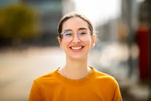 Woman wearing glasses and smiling while standing on a street