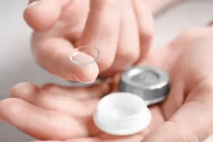 Hands holding a contact lens and a small silver contact lens case