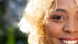 A smiling woman with curly blonde hair, possibly in a garden, with her eyes closed and a slight smile on her face.