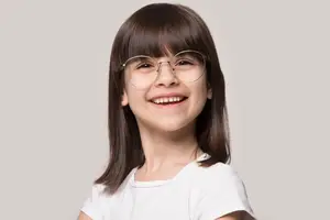 A smiling girl with short hair wearing a white shirt and glasses with a gray background