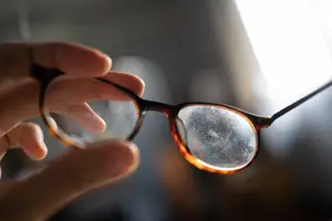 A hand holding a pair of glasses with a slight blur and a bright light source behind
