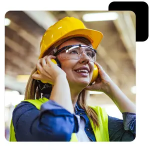 Image of a woman wearing a yellow hard hat, glasses, and a neon green vest with her hands on her ears