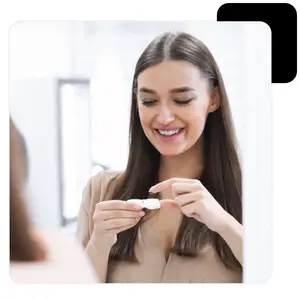 A woman is smiling and holding a contact lens case in her hand.