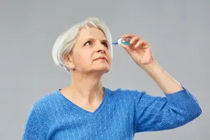 An elderly woman administering eye drops while looking upwards