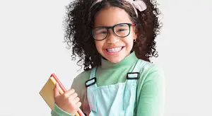 A young girl with curly hair wearing glasses and holding a book and pencils