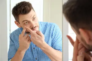 Man looking at himself in the mirror with a sore on his face