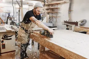A man using a power tool in a workshop while sawdust flies in the air
