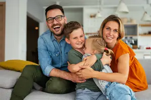 A family of four, a man, a woman, and two children, is sitting on a couch and smiling for a photo.