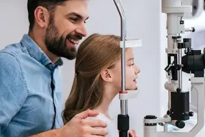 A young girl is having her eyes checked by a man in a white room