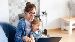 A woman and a child sitting on a couch in a living room with a laptop in front of them