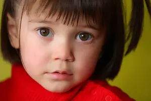 Close-up of a young girl with brown eyes and short hair wearing a red turtleneck against a yellow background