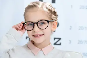 A little girl with glasses is looking at a wall with a letter Z and other letters behind her