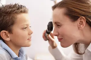 A woman is checking a boy's eyes with an ophthalmoscope