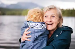 A happy elderly woman hugs a child on a lakeside in a serene and picturesque setting