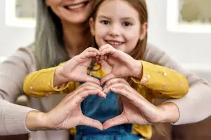 A woman and a young girl are smiling and posing for a photo with their hands forming a heart shape