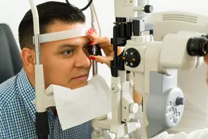 A man is having his eyes examined by an optometrist using a slit lamp in a clinic.