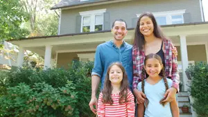 A family of four standing in front of their house, smiling at the camera.