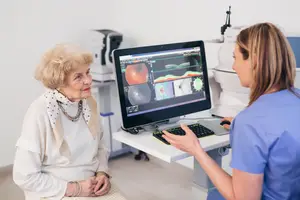 A female patient and an optometrist are reviewing an eye scan on a monitor.