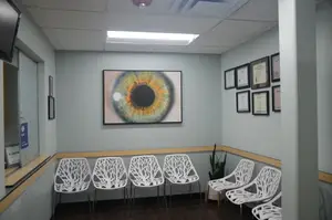 A medical room with white chairs, a framed eye picture, and certificates on the wall
