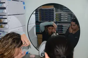 A group of women is gathered around a mirror, possibly in a laboratory, with one woman holding a piece of food in her hand, while another woman is touching her face with her hand and the other woman is holding a pen.