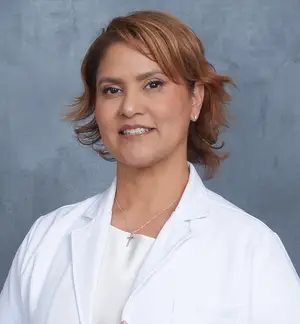 A woman with short hair is smiling and posing for a photo while wearing a white lab coat and a necklace.