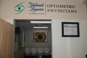 The entrance to an optometrist's office with chairs, a monitor, and a framed poster on the wall.